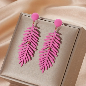 Macro shot of matte rose pink leaf-shaped dangle earrings on golden silk background