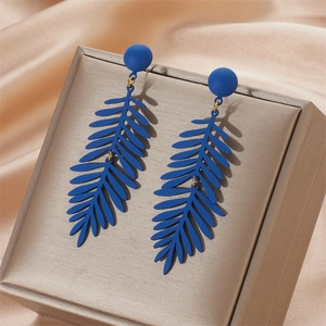 Macro view of long dark blue leaf drop earring with hollow matte finish on silk cloth
