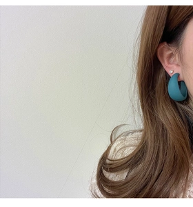 Close-up of matte blue geometric C-shaped earrings and crystal stud on model