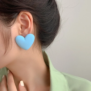 Macro shot of light blue matte heart stud earrings on model with green shirt