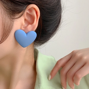 Close-up of a model wearing matte light blue heart stud earrings with a 925 silver needle