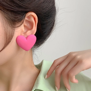 Close-up of a large matte pink heart earring worn on ear with soft artistic lighting