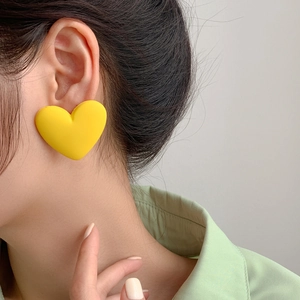 Close-up of bright yellow matte heart stud earrings worn by a model in a mint green shirt
