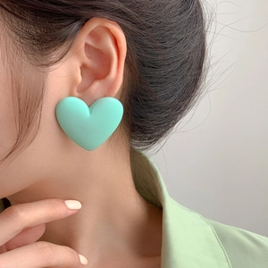 Close-up of a model wearing large mint green matte heart stud earrings in 925 silver