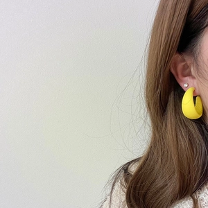 Matte yellow C-shaped hoop earrings with stud detail on a model's ear for fashion