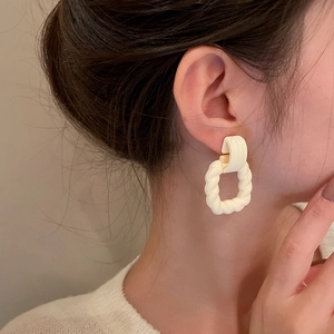 Detailed view of matte cream twisted geometric C-shape earrings on a model with knitwear