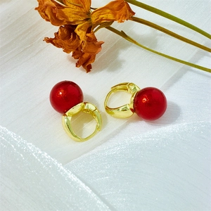 Classic gold hoop earrings with red pearl pendants on a white textured fabric background