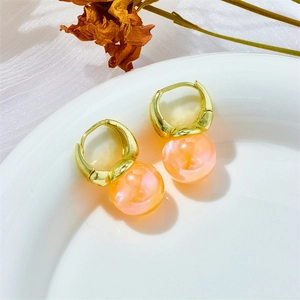 Detail of peach mermaid pearl hoop earrings with golden finish on a white ceramic plate