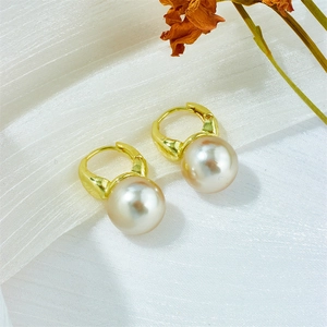 Detail view of pearlescent mermaid pearls on elegant gold hoop earrings on white fabric