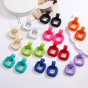 Array of colorful matte twisted hoop earrings in candy colors on white ceramic plates