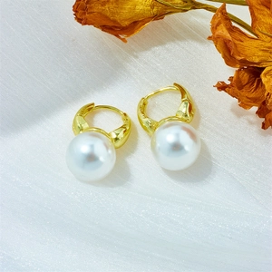 Detail of gold hoop earrings with white round pearls on light textured fabric background