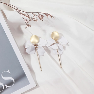 Close-up of white 3D flower petal earrings with gold dangling rods on soft white fabric