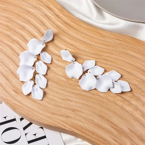 Detail of white matte petal earrings with gold chain on a textured wooden tray