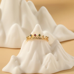 Anillo de corona dorado con piedras de circón de colores en soporte de cerámica blanca