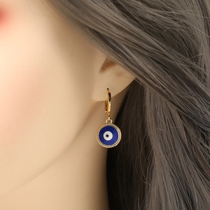 Golden hoop earrings with blue enamel evil eye charms worn by a female model