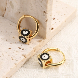 Detailed close-up of golden square cube evil eye charm hoop earrings on a textured surface