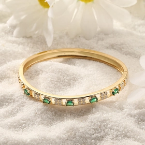 Detail van gouden open armband met groene zirkonia en witte klaverpatronen op zand