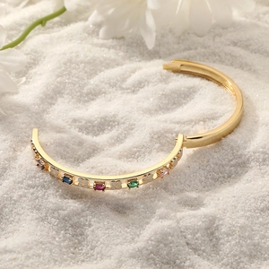 Detail van gouden scharnierarmband met kleurrijke stenen en wit geëmailleerde klavers