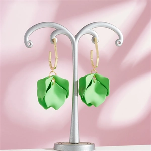 Macro shot of green petal earrings with golden hexagon studs on a pink display stand