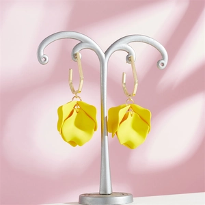Detail of yellow petal earrings with golden geometric hooks on a metal jewelry stand