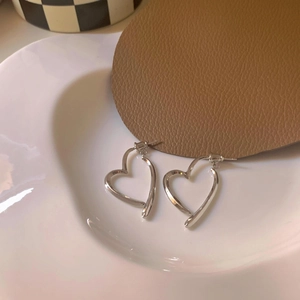 Elegant silver hollow heart earrings with metal cross design on a white ceramic plate