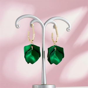 Close-up of green petal drop earrings with gold hexagonal studs on a silver display