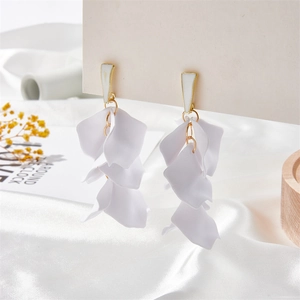 Macro shot of tiered white petal tassel earrings with gold metal accents on silk