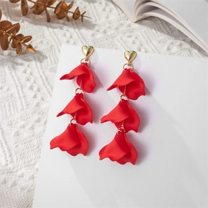 Detail of red long petal drop earrings with golden heart studs on white fabric background