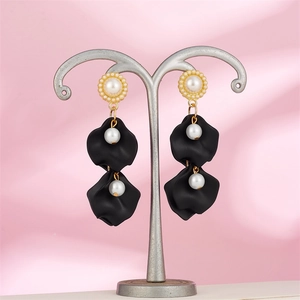 Detail of long drop earrings featuring matte black petals and white pearls on a silver stand