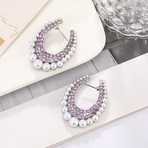 Detailed view of U-shaped silver earrings with purple rhinestones and white pearls