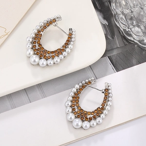 Macro shot of silver C-shaped earrings featuring amber rhinestones and white pearls