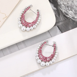 Macro detail of silver C-shaped earrings with pink zircons and white pearls on a tray