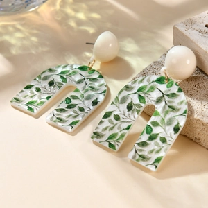 Detail of U-shaped acrylic earrings with green leaf pattern and white marble texture