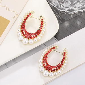 Detailed view of C-shaped gold earrings with red rhinestones and gradient white pearls