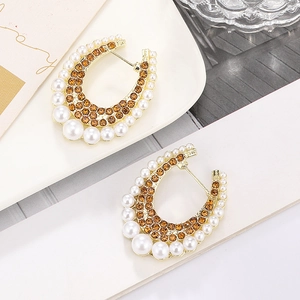 Detail of horseshoe earrings with amber rhinestones and pearls on a white plate