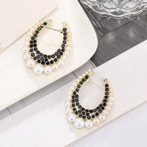 Macro shot of U-shaped earrings with black crystals and pearls on white ceramic