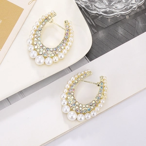 Chunky gold U-shaped earrings with colorful rhinestones and pearls on white plate