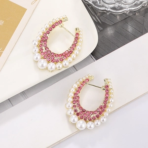 U-shaped gold earrings with pink rhinestones and gradient faux pearls on a white plate