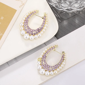 Detail of U-shape gold earrings with purple crystals and pearls on a white plate