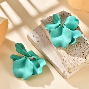 Macro detail of mint green matte petal earrings on a textured stone surface with shadows