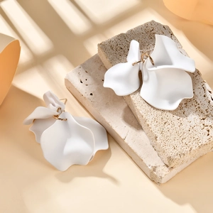 Close-up of white petal earrings with golden hooks on stone under window shadows