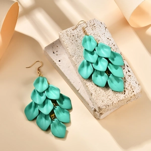 Close-up of mint green petal tassel earrings on a textured stone and beige background