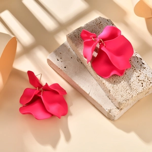 Macro shot of stylish matte rose pink petal earrings on a beige textured stone base