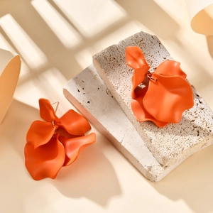 Detailed macro view of orange layered petal earrings with matte lacquer finish on beige stone