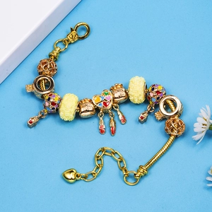 Gold beaded snake chain bracelet with heart, fortune bag and feather charms on blue fabric