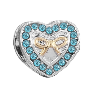 Macro shot of silver heart charm with blue crystals and a gold bow for DIY bracelets