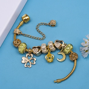 Golden charm bracelet with heart, crown, and clover pendants on blue background