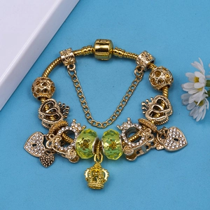 Gold beaded charm bracelet with green glass stones and crown pendants on a snake chain