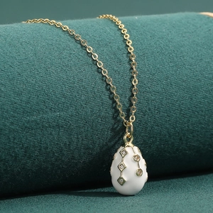 18K gold plated copper necklace with white enamel egg pendant on a green velvet stand