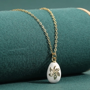 Exquisite 18K gold O-chain necklace with white enamel egg pendant on green velvet
